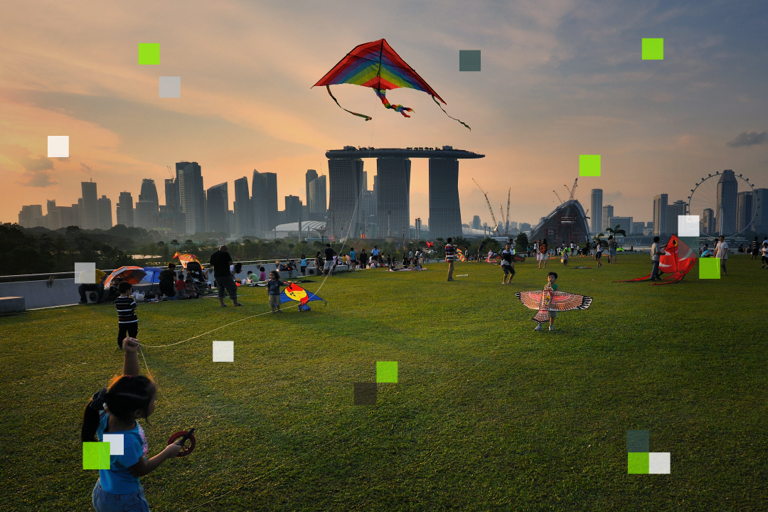 Families flying kites with Marina Bay Sands in the background during sunset.